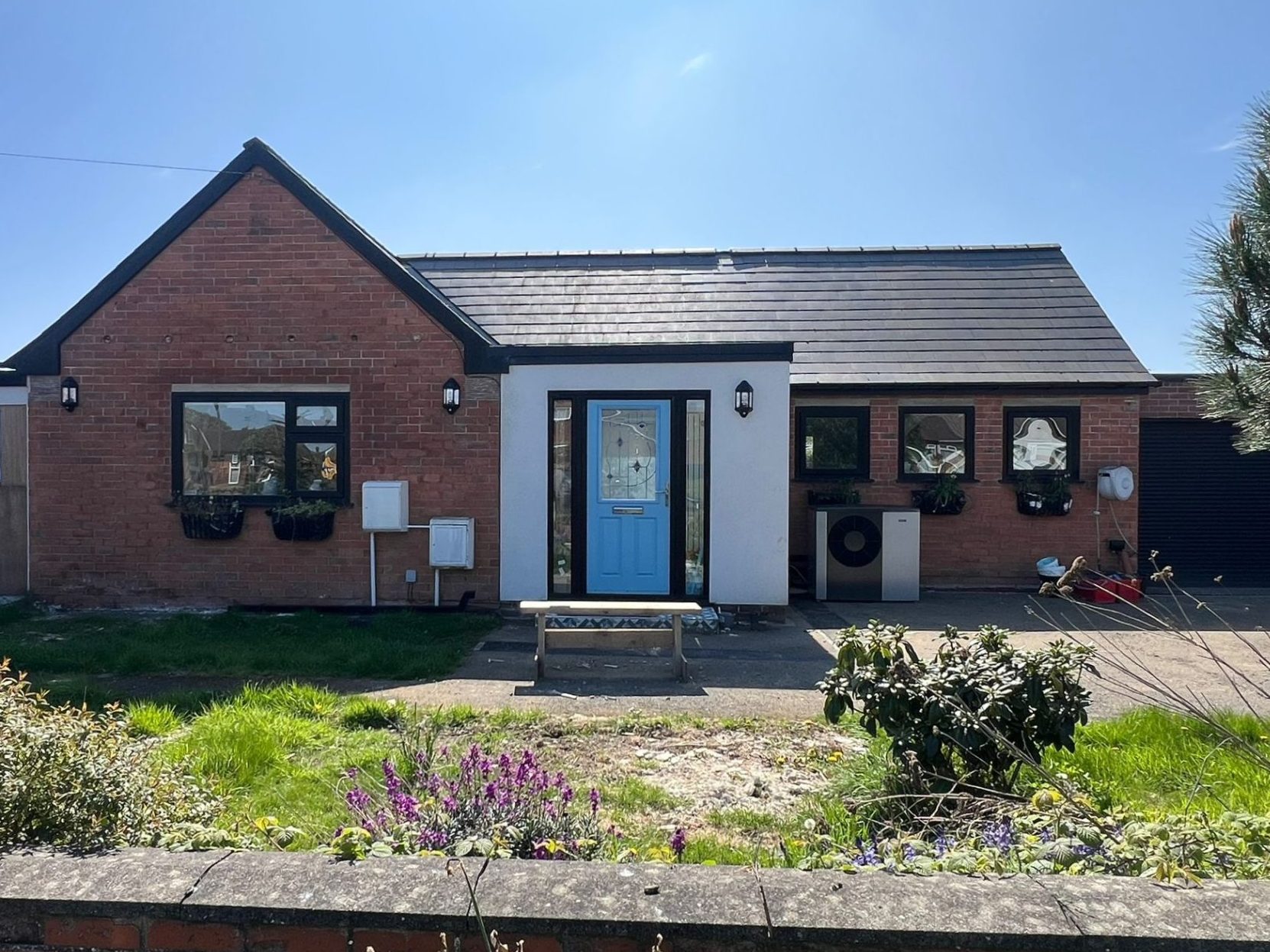 Photo of bungalow in sunshine with newly installed heat pump outside